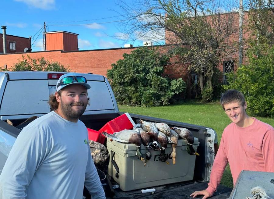 Two hunters at an open truck tailgate with mallards, a wood duck and a bufflehead across the cooler